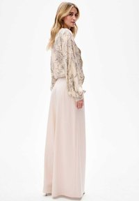 Lichte, bloemengepatroneerde crèmekleurige blouse met puffmouwen, gecombineerd met luchtige, lichtroze wijde broek, wat een zachte silhouet creëert.