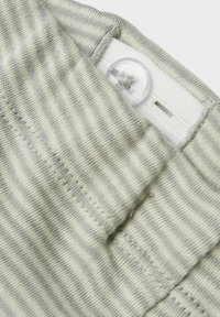 Close-up van lichtgrijs gestreept stof met een duidelijke knop bevestigd aan een verstelbare elastische band voor het aanpassen van de maat van kleding.