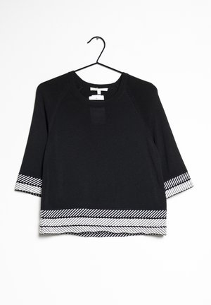 Pull noir à manches trois-quarts avec bordure à rayures diagonales blanches aux poignets et à l'ourlet, suspendu sur un cintre en fil de fer noir sur fond blanc.