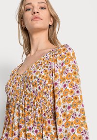 Vestido floral com corpete franzido, apresentando flores laranja, rosa e brancas. Mangas longas bufantes com punhos elásticos. Tecido macio.