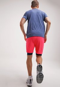 Conjunto deportivo que incluye una camiseta de manga corta azul y pantalones cortos rosas. Zapatillas deportivas grises con detalles en negro y blanco. Enfocado en la comodidad y el movimiento.