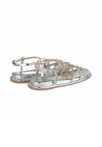 Zilveren metallic sandalen met kruislings straps en een gespsluiting rond de enkel. Gladde afwerking met een platte zool en lichte tan accenten.