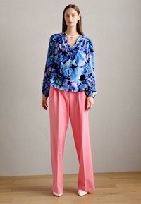 Blusa a fiori nei toni del blu, viola e verde, abbinata a pantaloni rosa a vita alta. Completa il look un paio di décolleté bianchi a punta.
