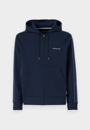 Haut à zip bleu marine en tissu doux, avec une capuche à cordon, deux poches avant et des bandes latérales contrastées avec un détail de logo.