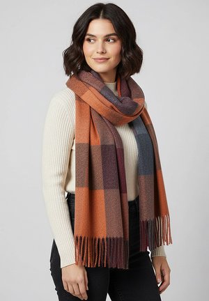 Brown and gray plaid scarf made of soft fabric, featuring fringed ends and a cozy drape, worn over a cream-colored ribbed sweater.