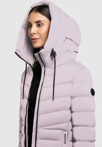 Pufová bunda v svetlej levandulovej farbe, s vysokým golierom, veľkou kapucňou a čiernymi šnúrkami. Prešité prevedenie s predným zipsom.