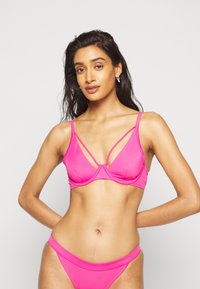 Conjunto de bikini rosa com um bralette apresentando alças cruzadas. Tecido liso e elástico; cobertura mínima com um design sem costuras.