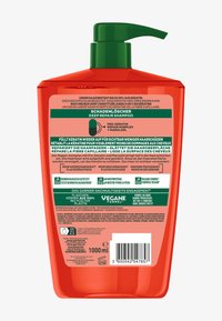 Bouteille de shampooing en plastique rouge avec une pompe verte. L'étiquette présente du texte en plusieurs langues, détaillant les ingrédients et l'utilisation. Volume : 1000 ml.