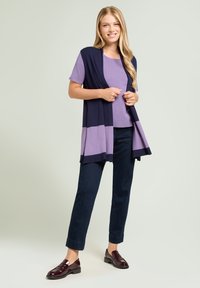 Cárdigan en bloques de color azul marino y lavanda sobre una blusa lavanda, combinado con pantalones oscuros y zapatos burdeos. Telas suaves, ajuste relajado.