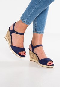 Námořnické modré semišové klínové sandály s otevřenou špičkou, nastavitelným páskem kolem kotníku a klínovým podpatkem s korkovou texturou.