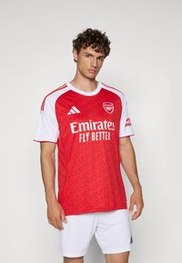 Rode en witte voetbalshirt met een textuurpatroon, korte mouwen, ronde hals en branding voor Arsenal en Emirates.