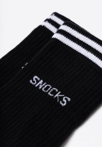 Zwarte katoenen sokken met witte strepen aan de bovenkant. Het woord "SNOCKS" is prominent afgebeeld in witte letters aan de zijkant.