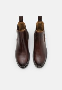 Ein Paar polierte dunkelbraune Leder-Chelsea-Stiefel mit Zuglaschen, von oben auf einem weißen Hintergrund betrachtet.