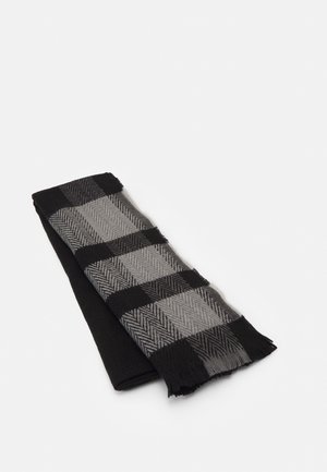 Écharpe pliée à carreaux noirs et gris avec un motif en chevrons sur fond blanc.