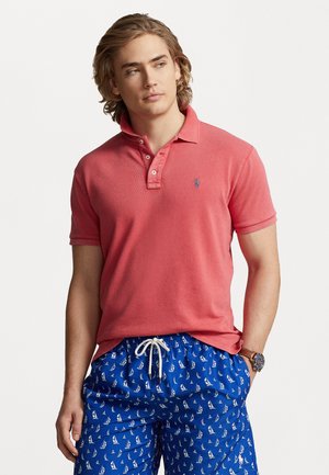 Polo de color rosa claro con cuello y tres botones, combinado con pantalones cortos azules con un patrón de veleros en blanco, fabricados con tela suave.