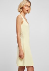 Vestido sin mangas de color amarillo claro con escote redondeado, textura suave y forma acampanada, que presenta costuras laterales sutiles y un corte a la altura de la rodilla.