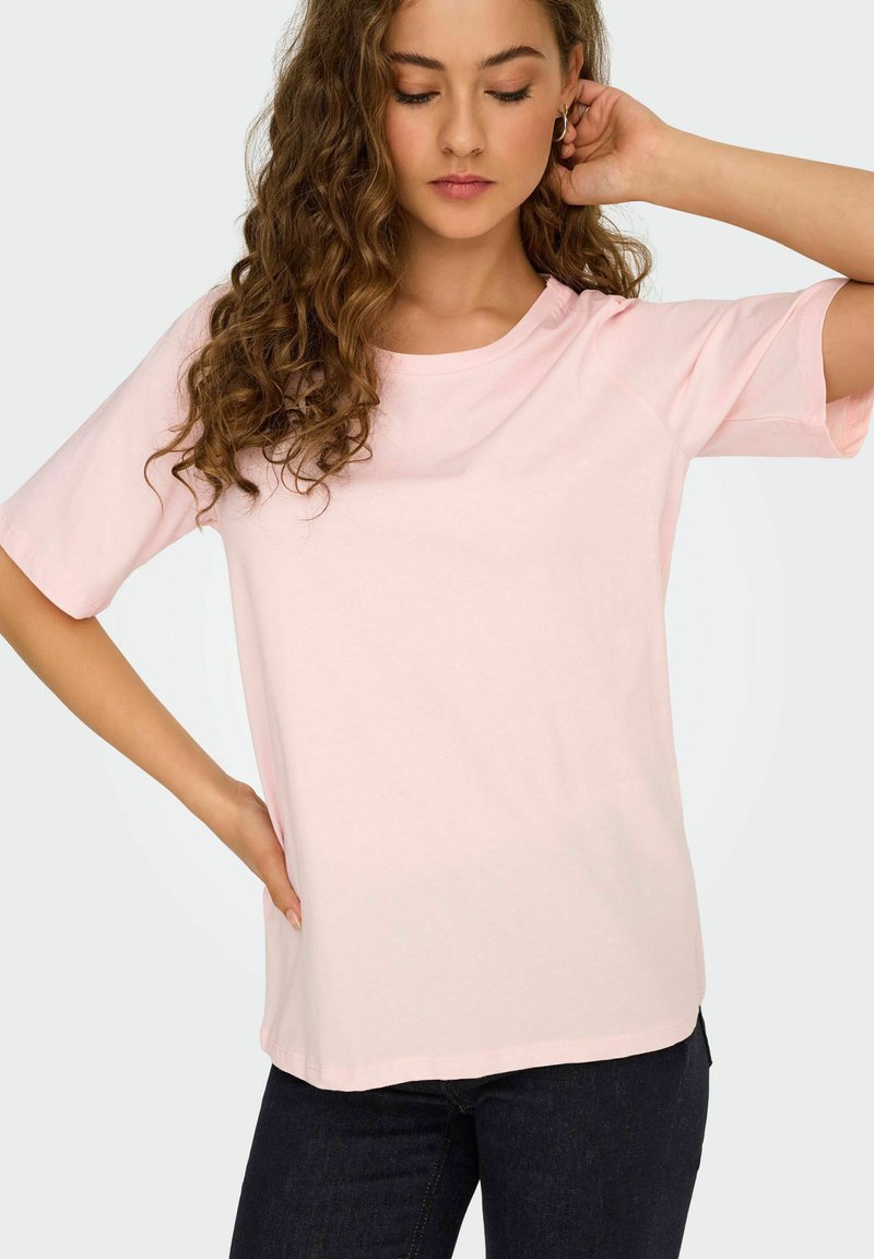 Lyserød t-shirt med korte ærmer i blød bomuld med rund halsudskæring og løs pasform. Har rullede ærmer og en subtil sømdetalje.
