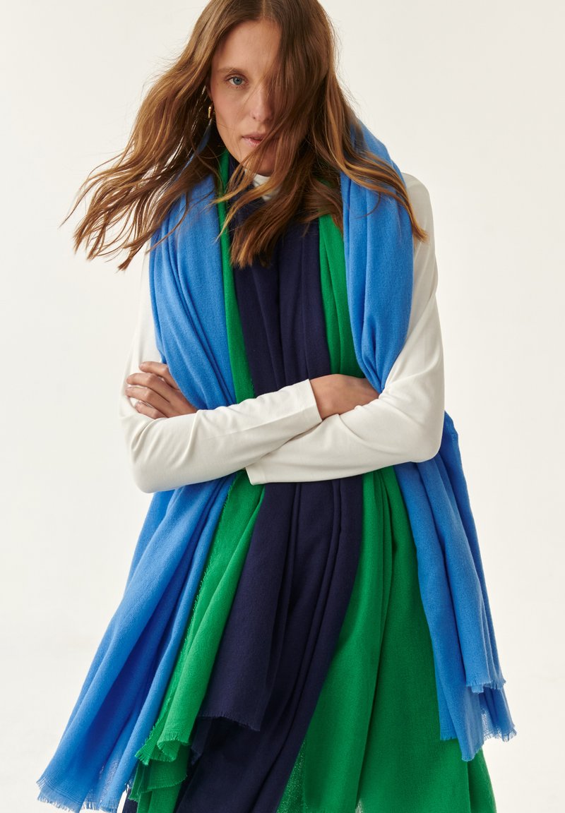 Sciarpa multicolore con pannelli blu, verde e navy. Realizzata in morbido tessuto con bordi frangiati, drappeggiata con stile sulle spalle del modello.