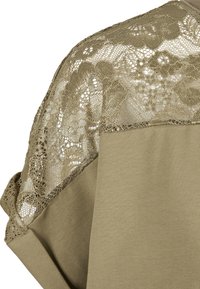 Tissu beige avec détail en dentelle florale sur l'épaule et le haut de la manche d'un vêtement.