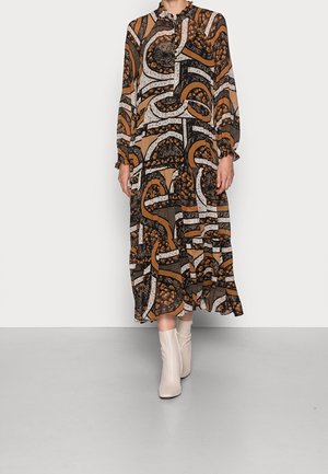 Bruine maxi-jurk met patroon, lange mouwen en ruches aan de manchetten, met krullen en texturen, gecombineerd met crème kniehoge laarzen.