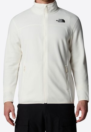 Mand iført en hvid fleecejakke med lynlås med The North Face-logo på brystet og sorte bukser med cargolommer.