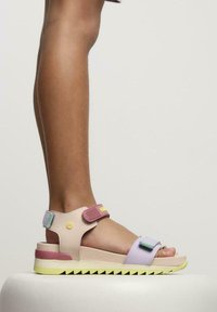 Sandale multicolore avec une sangle ajustable rose, des accents violets et verts, une semelle en mousse avec un fond jaune, et un design en zigzag.