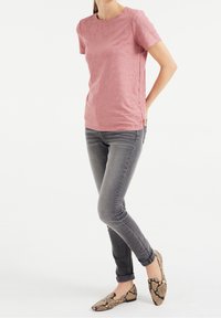 Růžové triko s krátkým rukávem a kulatým výstřihem, spárované s šedými slim-fit džíny a mokasínami se vzorem hada.