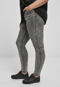 Szürke, elhasználódott mosású, skinny farmernadrág, ami slim fit szabású, varrási részletekkel rendelkezik, közepes magas derékkal, fekete sportcipővel párosítva.
