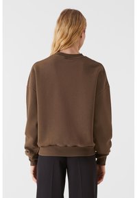 Pulover oversized maro, cu guler și manșete cordonate; are o textură moale și mâneci lungi. Designul este simplu și are o croială lejeră.