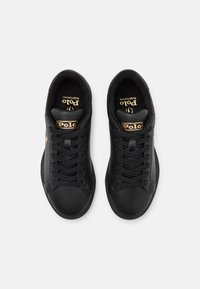 Černé kožené tenisky s nízkým střihem, kulatou špičkou, černými tkaničkami a zlatým logem "Polo" na jazyku. Měkká vnitřní podšívka.