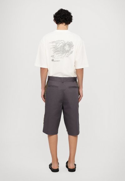 White oversized t-shirt with graphic print on back, paired with gray shorts featuring leopard print side panels. Black sandals on feet.