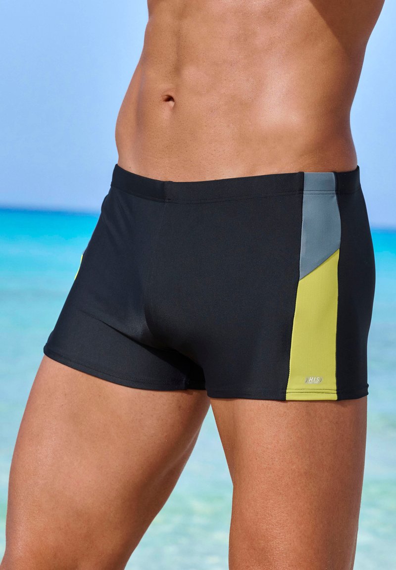 Schwarze Schwimmshorts aus elastischem Material mit einem Design aus grauen und leuchtend gelben Seitenpaneelen. Glatte Textur mit einem elastischen Bund.