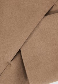 Gros plan d'un tissu en laine beige avec des coutures qui se chevauchent et des détails de couture visibles.