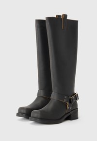 Botas negras hasta la rodilla de cuero suave con una forma ajustada, costuras de acento marrón, una correa con hebilla y un tacón grueso.