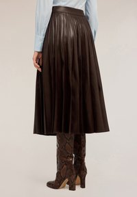 Falda de cuero marrón con plisados y una cintura alta, combinada con botas de rodilla de estampado de serpiente marrón. Textura suave, longitud a medio pantorrilla.