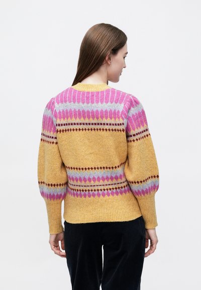 Megztinis, pasiūtas iš geltonos spalvos pagrindo su rožiniais ir pilkais geometriniais raštais, pūstomis rankovėmis ir kantuotu iškirpte bei apačia. Minkšta vilnos tekstūra.