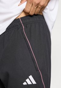 Γκρι αθλητικό παντελόνι με υφή, με ροζ κάθετη ρίγα στο πλάι και λευκή λεπτομέρεια λογότυπου. Ελαστική μέση για ρυθμιζόμενη εφαρμογή.