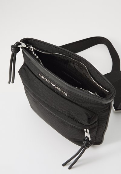 Geantă crossbody neagră Emporio Armani, cu buzunar frontal cu fermoar, fermoare argintii cu ciucuri din piele și curea ajustabilă, pe fundal alb.