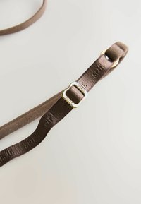 Pruun kangas rihm särava kuldse tooni pildi ja väljapressitud brändingu, millel on lame kujundus ja sile tekstuur.