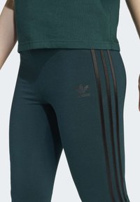 Teal legice s črnim dizajnom treh črt, s subtilnim črnim logotipom na stegnu. Narejene iz raztegljivega, oprijetega materiala.