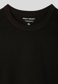 T-shirt nera di peso pesante con collo rotondo. L'etichetta reca la scritta "HEAVY WEIGHT" e "TERRANOVA", taglia XL, con un tessuto liscio e texturizzato.