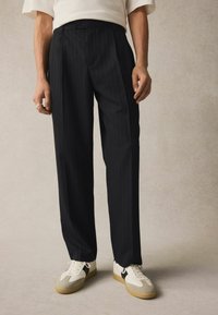 Pantalons noirs à rayures avec une devant plissé, coupe ajustée et poches latérales, associés à des baskets blanches avec des accents gris.