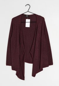 Kastanjefärgad öppna cardigan med långa ärmar och chevronmönster som hänger på en svart galge mot en vit bakgrund.