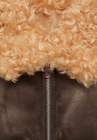 Jachetă din suede căprui, dotată cu un guler din fleece moale, creț, de culoare portocalie deschisă și un fermoar argintie pe față. Materiale texturate și vizual contrastante.