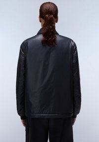Zwarte, glanzende pufferjack met een relaxte pasvorm, rugventilatie en ribgebreide mouwen. Heeft een minimalistisch ontwerp en een soepele textuur.