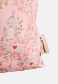 Rózsaszín anyag virág- és szívmintákkal, apró rajzfilmszereplő illusztrációkkal és egy bézs címkével, amelyen az olvasható: "Cath Kidston x MOOMIN."