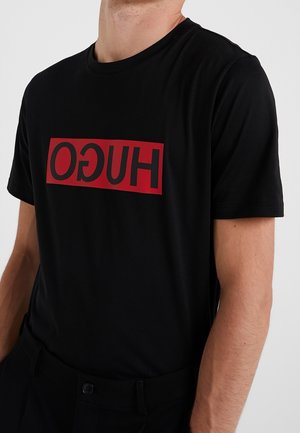 Czarna koszulka z bawełny z okrągłym dekoltem, zdobiona czerwonym prostokątnym logo z napisem "HUGO" w czarnym kolorze.