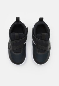 Zwarte sportieve schoenen met bovenwerk van mesh, klittenbandsluiting, gevoerde kraag en witte rubberen loopzool. Lichtgewicht ontwerp voor comfort.