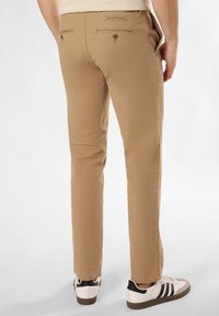 Chinos kaki avec une texture lisse, coupe ajustée et deux poches arrière. Présente des accents de boutons marron et est porté avec des sneakers blanches.