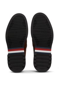 Schwarze Gummisohlen mit strukturierten Mustern und Rillen. Mit einem gestreiften Akzent in Rot, Weiß und Blau nahe der Ferse.